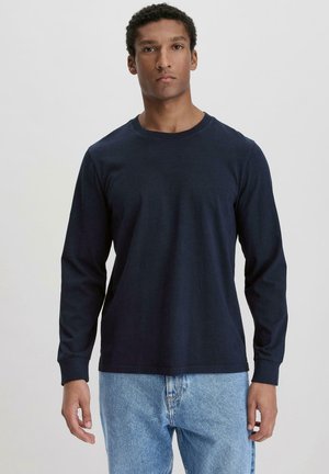 Marineblauwe langemouw t-shirt van zacht materiaal met een ronde hals en geribbelde manchetten, gecombineerd met lichtblauwe spijkerbroek.