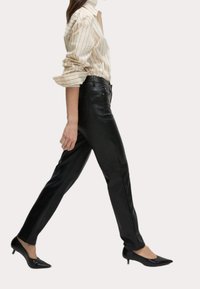 Svarta läderbyxor med slim fit, utrustade med framfickor och en mjuk yta. Kombinerat med en beige randig skjorta med knappar och svarta klackar.