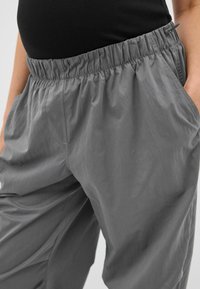 Pantalons gris légers avec une taille élastique, dotés de poches latérales et d'une coupe décontractée, fabriqués en tissu lisse et légèrement brillant.