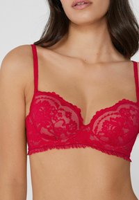 Červeno krajkový bralette s květinovým vzorem, vlnkovanými okraji a nastavitelnými ramínky. Obsahuje průsvitné síťované detaily a lehce vyztužené košíčky.