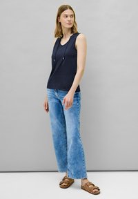 Top senza maniche di colore blu navy con scollo rotondo e dettaglio con cordini, abbinato a jeans ampi di colore azzurro chiaro e sandali marroni con pois.