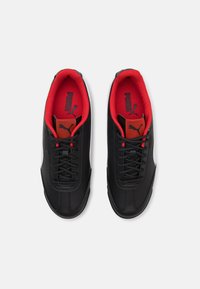 Chaussures de sport noires avec dessus en cuir lisse, doublure textile rouge contrastante, accents latéraux blancs et lacets noirs. Présentent un logo sur la languette.