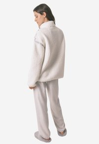 Biały polarowy pulower z wysokim kołnierzem, szarymi akcentami i luźnym krojem, w połączeniu z jasnoszarymi miękkimi spodniami i pluszowymi klapkami.