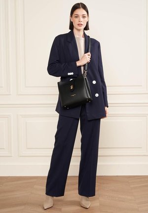 Borsa a tracolla in pelle nera con una chiusura dorata, abbinata a un blazer scuro, una maglietta chiara e pantaloni a gamba larga. Tacchi neutri completano l'outfit.