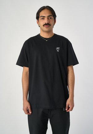 Schwarzes Baumwoll-T-Shirt mit rundem Halsausschnitt, kurzen Ärmeln und einem kleinen weißen gestickten Design auf der linken Brust.