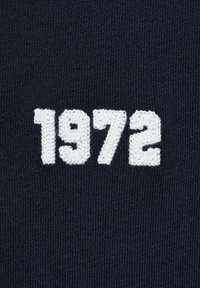Námořnická tkanina s texturovaným pletením, na které jsou uprostřed a mírně vyvýšeně vyšívané bílé číslice "1972", což vytváří výrazný kontrast.