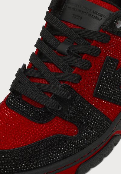 Gros plan sur une basket rouge et noire avec des lacets noirs et un matériau texturé recouvrant la tige et le bord de la semelle.