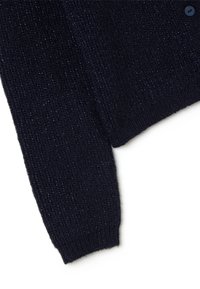 Sezione di cardigan lavorato a maglia blu navy con texture a coste e polsini; presenta fili lucenti per un tocco in più; un pulsante blu visibile.