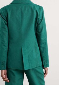 Blazer verde acqua con colletto a revers, vestibilità su misura e polsini con tre bottoni. Tessuto morbido con spacco centrale posteriore per un facile movimento.