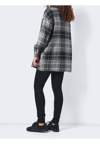 Czarna i szara koszula w kratę z długim rękawem, uszyta z miękkiego materiału, zestawiona z czarnymi legginsami i czarnymi sneakery. Projekt zawiera mankiety zapinane na guziki.