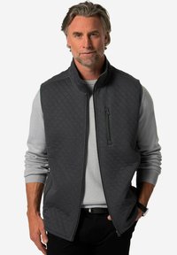 Mörkgrå kviltad väst med hög krage, en dragkedjeförsedd bröstficka och sidofickor, lagrad över en ljusgrå tröja. Slät textur.