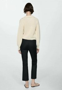 Beige gebreide trui met een kraag, gecombineerd met zwarte cropped pants. De outfit wordt afgewerkt met platte sandalen.