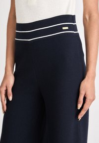 Ναυτικά παντελόνια με φαρδιά ποδιά και ραβδωτή υφή, με ψηλή μέση που διαθέτει λευκές λεπτομέρειες και ένα μικρό χρυσό λογότυπο στο πλάι.