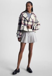 Cropped, cream plaid jacket with burgundy and navy accents, double-breasted buttons, paired with a pleated light gray skirt and black loafers.