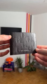 Portefeuille en cuir noir avec un motif géométrique embossé et le nom "KARL LAGERFELD" en lettres argentées en bas.