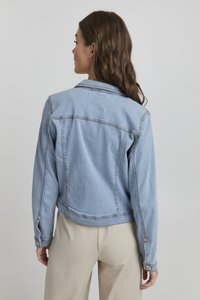 Ljusblå denimjacka med en kortad design, avslutad med synliga sömmar och knappdetaljer på ärmarna. Slät yta.