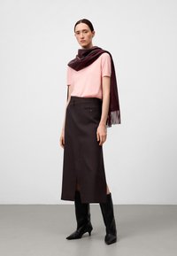 Roze shirt met korte mouwen, donkerbruine rok tot de knie met een split aan de voorkant, en een kastanjebruine sjaal. Zwarte kniehoogte puntige laarzen. Minimalistische achtergrond.