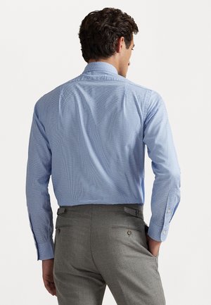 lichtblauw geruite blouse met lange mouwen en een spreadkraag, gecombineerd met grijze broek met twee achterzakken en knoopaccenten.