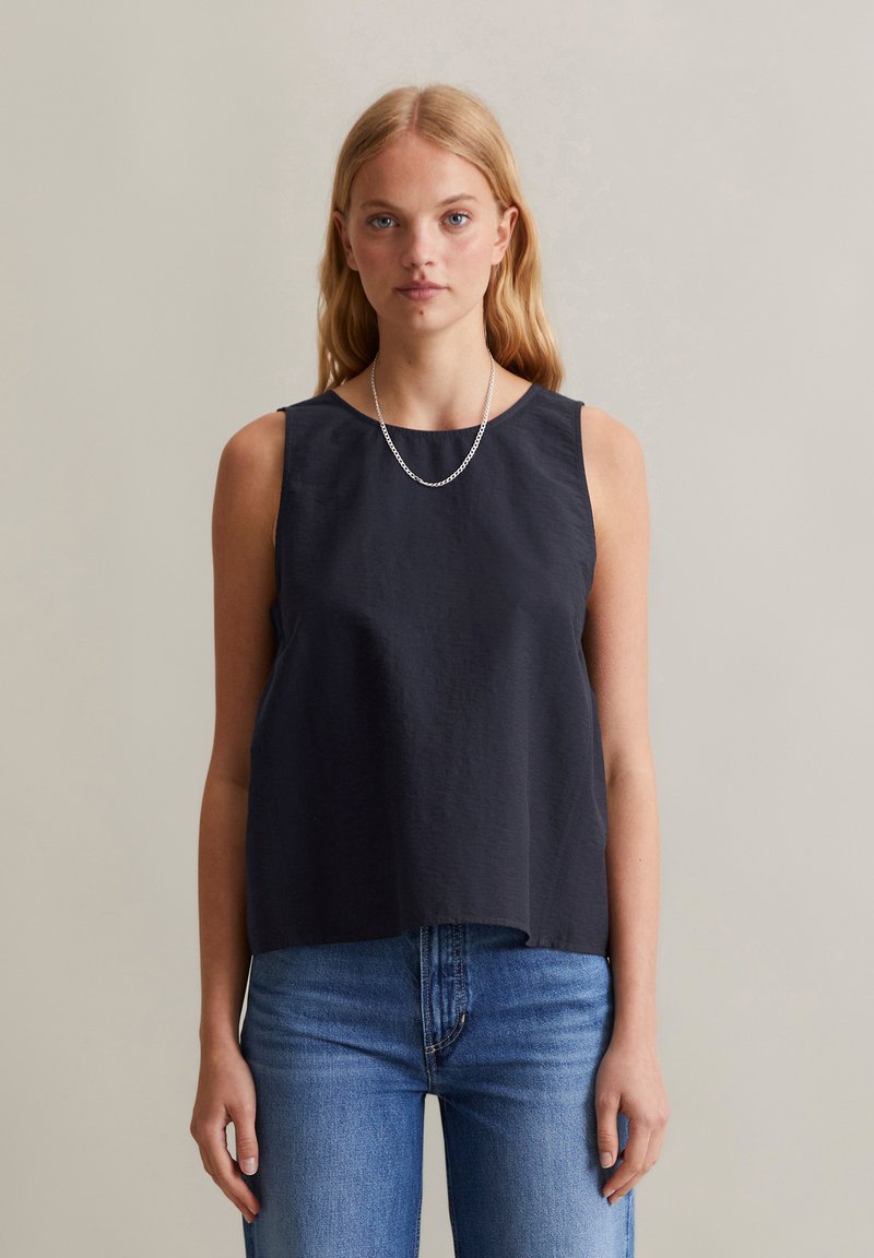 Donker marineblauw mouwloos topje met een ronde halslijn, gemaakt van textuurstof, gecombineerd met lichtblauwe jeans. Heeft een ontspannen pasvorm en een minimalistisch ontwerp.