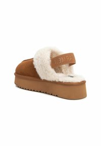 Zapatillas de plataforma de ante marrón con un grueso forro de lana blanca y una correa elástica con marca en la parte posterior para el soporte del talón.
