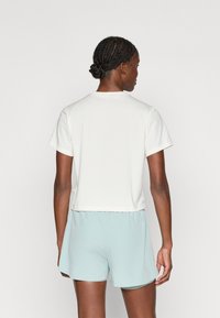 Rövid ujjú, laza fazonú, törtfehér anyagú felső, világoskék rövidnadrággal párosítva. Kerek nyakkivágással és finom varrási részletekkel rendelkezik.