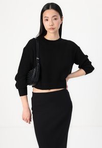 Μαύρο ριγέ πλεκτό πουλόβερ με cropped σχέδιο και στρογγυλή λαιμόκοψη, συνδυασμένο με μια μαύρη εφαρμοστή φούστα. Τονίζεται από μια μικρή τσάντα με τρουκς που φοριέται χιαστί.