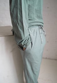 Zelená dlouhá rukávová košile a pruhované tepláky mají volný střih, měkký bavlněný materiál a elastický pas se šňůrkou.