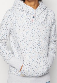 Jasnoszara bluza z kapturem o heatherowej teksturze, z powtarzającym się wzorem liści w odcieniach niebieskiego i różowego, kangurzą kieszenią i kapturem.