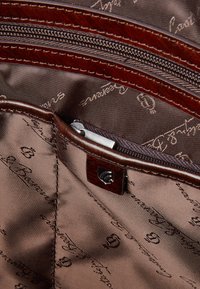 Brown leather bag interior with a zippered pocket; smooth fabric lining features repeated text pattern; accented with dark red stitching.