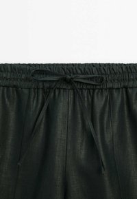 Pantalon noir à taille élastique avec un nœud en tissu à l'avant et des détails discrets de coutures verticales.