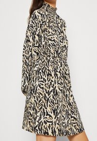 Animal-print dress featuring a high smocked collar, long sleeves, elastic waist, and a relaxed fit. Colors include black, beige, and cream.