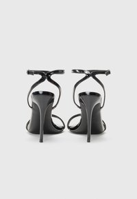 Schwarze Lackleder-High-Heelsandalen mit dünnem Knöchelriemen und gekreuzten Vorderbändern, ausgestattet mit einem schlanken Stiletto-Absatz.