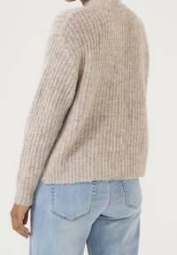 Suéter tejido de color beige claro con textura de canalé y cuello alto. Combínalo con pantalones vaqueros de mezclilla azul, que presentan un ajuste relajado.