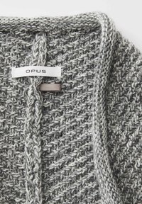 Grau gestrickter Schal mit einem strukturierten Muster. Verfügt über ein Etikett mit der Aufschrift "OPUS" und einem kontrastierenden, weichen Stoffakzent in der Nähe des Verschlusses.