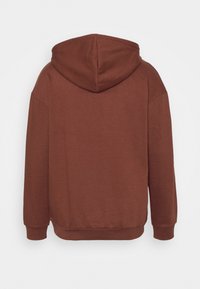 Brun hettegenser med en myk tekstur, som har en romslig hette, lange ermer og ribbestrikkede mansjetter og kant. Baksiden er enkel uten detaljer.