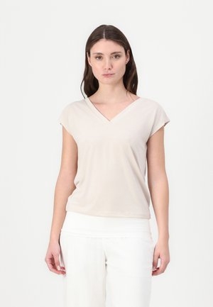 T-shirt beige à col en V et manches courtes, fabriqué en tissu doux, présentant une coupe décontractée et une texture lisse. Associé à un pantalon blanc.