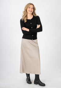 Czarny prążkowany kardigan z okrągłymi guzikami, zestawiony z gładką beżową satynową spódnicą i czarnymi masywnymi botkami za kostkę, stojący na białym tle.