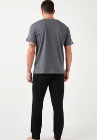 Camiseta de algodón gris con mangas cortas, que presenta un ajuste holgado. Combinada con pantalones de lounge negros y ajustados. Diseño simple sin patrones visibles.