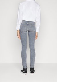 Jeans ajustados de mezclilla gris claro, con cintura alta, bolsillos traseros y una silueta entallada, combinados con zapatillas negras altas.