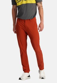 Heren slim-fit broek in fel oranje, gemaakt van gladde stof, met een rits, zijzakken en gecombineerd met witte sportschoenen.