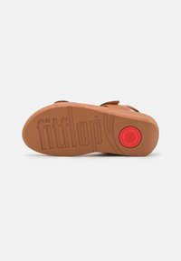 Tan gumená podošva s vyrazeným nápisom "fitflop". Obsahuje červený kruhový detail a textúrovaný povrch pre lepšie uchopenie. Ploché, otvorené prevedenie.