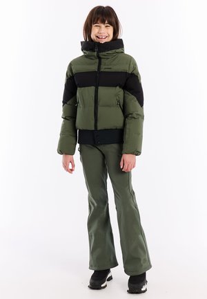 Grüne und schwarze Pufferjacke mit hohem Kragen, Reißverschluss und seitlichen Taschen, kombiniert mit grünen Hosen und schwarzen Schneestiefeln.