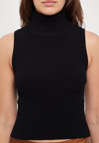 Top sin mangas negro de canalé con un diseño ajustado y textura suave, que presenta un cuello alto y costuras mínimas.