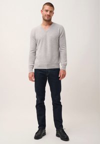 Suéter de punto gris claro con cuello en V y textura acanalada, combinado con jeans azul oscuro y zapatos negros con cordones. Diseño simple y ajustado.