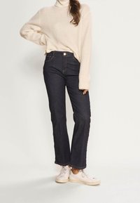 Maidonvalkoinen paksu neulepusero poolokauluksella ja pitkillä hihoilla, yhdistetty tummansinisiin, korkeavyötäröisiin liehulahkeisiin farkkuihin ja valkoisiin lenkkareihin.