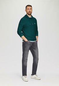 Turkusowy hoodie o teksturowanym wykończeniu i sznurkiem, w połączeniu z postrzępionymi, ciemnoszarymi dżinsami i białymi trampkami, z delikatnym detalem z logo.