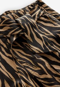 Tejido a rayas negras y marrones con un patrón texturizado, que presenta un detalle de cintura anudada y material suave y ligero.