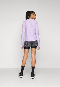 Langermet, lys lilla treningsgenser kombinert med mørke, mønstrede shorts. Har tettsittende design, elastisk stoff og sporty detaljer.