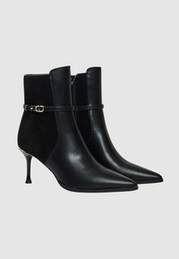 Stivaletti neri alla caviglia in pelle e camoscio. Punta affusolata, tacco sottile, chiusura con zip e cinturino decorativo con fibbia dorata.