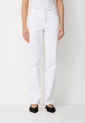 Woman wearing white straight-leg jeans, white sleeveless top, and black pointed-toe flat shoes, standing against a white background.